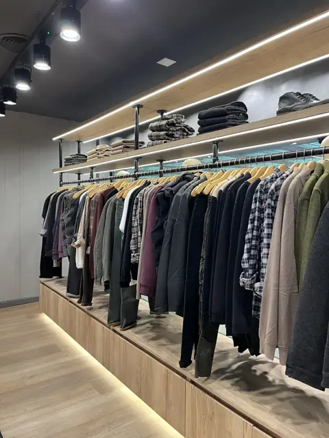 Exhibidores de pared a medida con base de madera iluminada y percheros de hierro para local de indumentaria